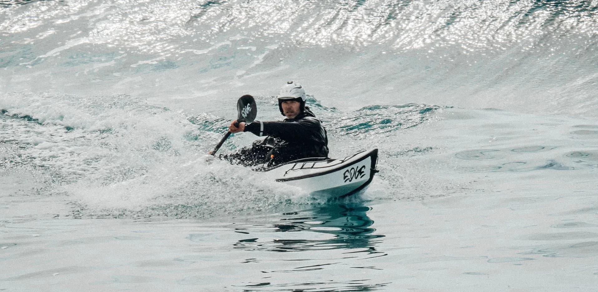 Mann sitter i kajakk og surfer på bølgene.